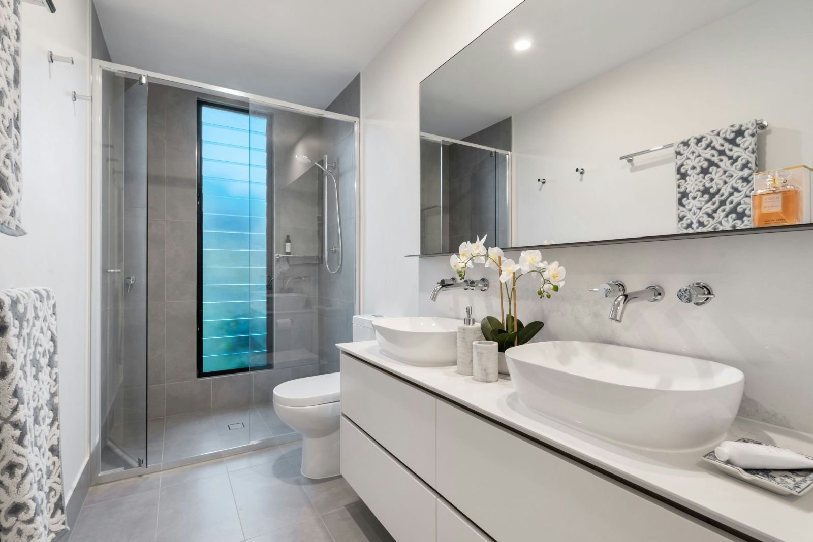 Badezimmer mit Glasdusche, Doppelwaschtisch in Weiß und grauen Fliesen